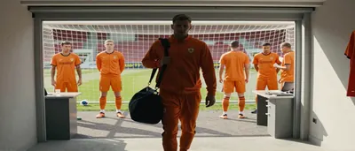 Kayne van Oevelen, 22, in a plain orange and white goalkeeper kit, diving dramatically to parry a high ball on a...