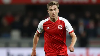 A photorealistic image of a young, anonymous FC Volendam player in a red jersey with white sleeves, running with the...
