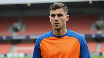 A determined FC Volendam midfielder, 25, with a strong build, wears a plain orange and blue training top, intense eyes...