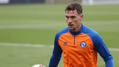 A determined, athletic FC Volendam midfielder, 25, in a vibrant orange and blue training top, fills the frame, soft...