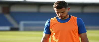 A 34-year-old defender with a rugged build, in a plain orange and blue training top, stands on the Kras Stadion pitchside...