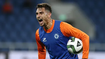 Mid-30s, lean forward-leaning FC Volendam winger, orange sleeves and blue torso training top, sweat-glazed skin, eyes...