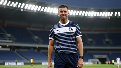 A photorealistic image of a 30-40 year old male coach in his mid-30s, wearing a dark blue and white striped shirt with a...