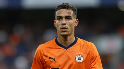 A young male footballer in his early 20s, wearing a solid orange Volendam kit, waist-up portrait with a blurred stadium...