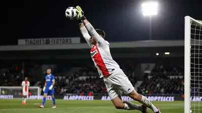 A 25-year-old Volendammer goalkeeper, wearing a white jersey with a red stripe, makes a spectacular save on a shot from a...